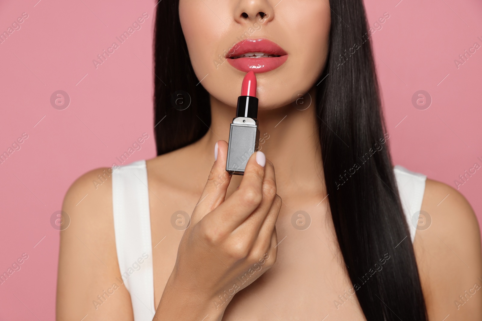 Photo of Young woman applying glossy lipstick on pink background, closeup