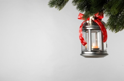 Photo of Vintage Christmas lantern with burning candle hanging on fir branch against light background. Space for text