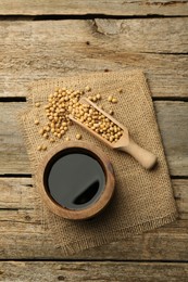 Soy sauce in bowl and soybeans on wooden table, flat lay