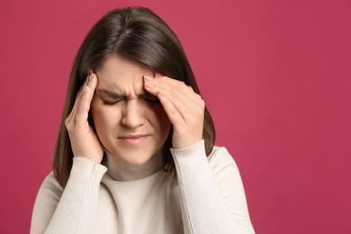 Photo of Young woman suffering from migraine on crimson background