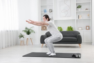 Photo of Senior man in sportswear doing exercises on mat at home