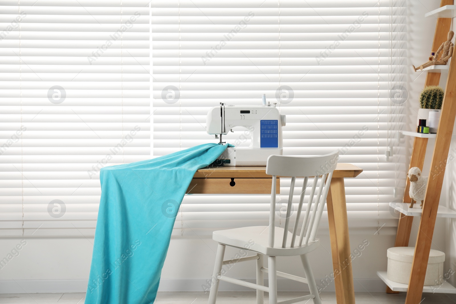 Photo of White sewing machine and fabric on wooden desk near chair indoors