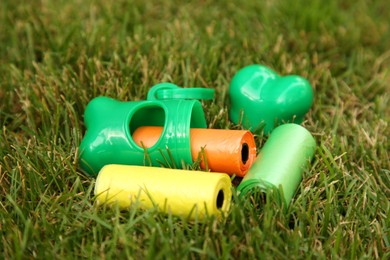 Photo of Rolls of colorful dog waste bags on green grass outdoors