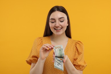 Photo of Happy woman with dollar banknotes on orange background