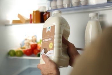 Image of Man holding gallon of coconut milk near refrigerator, closeup. Vegan product