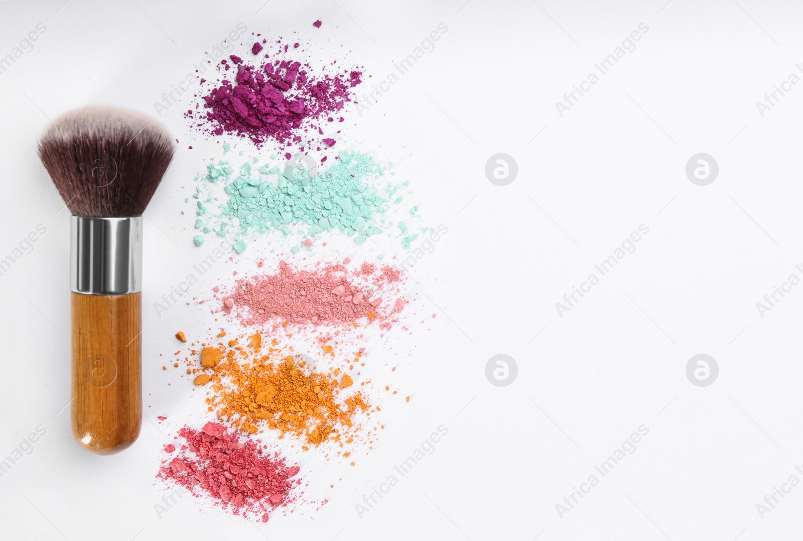 Photo of Makeup brush and scattered eye shadows on white background, flat lay. Space for text