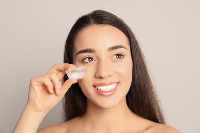 Young woman with ice cube on light background. Skin care