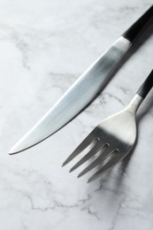 Photo of Stylish cutlery. Fork and knife on white marble table