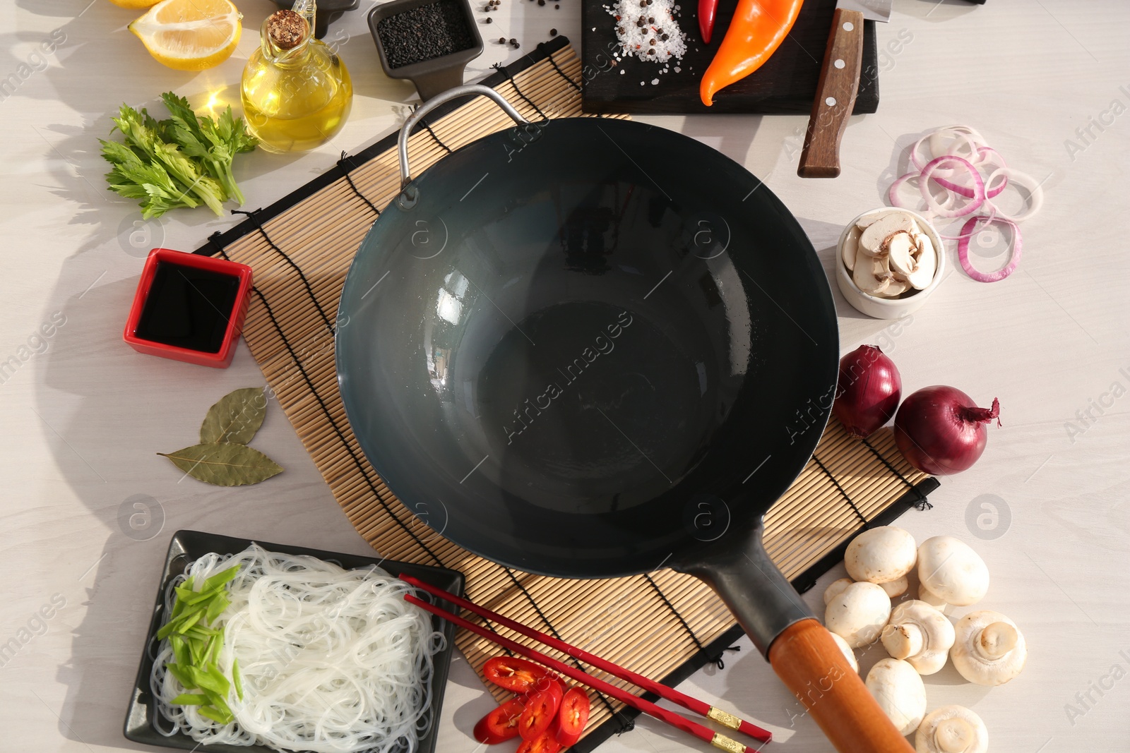 Photo of Wok, chopsticks and different products on white wooden table, flat lay