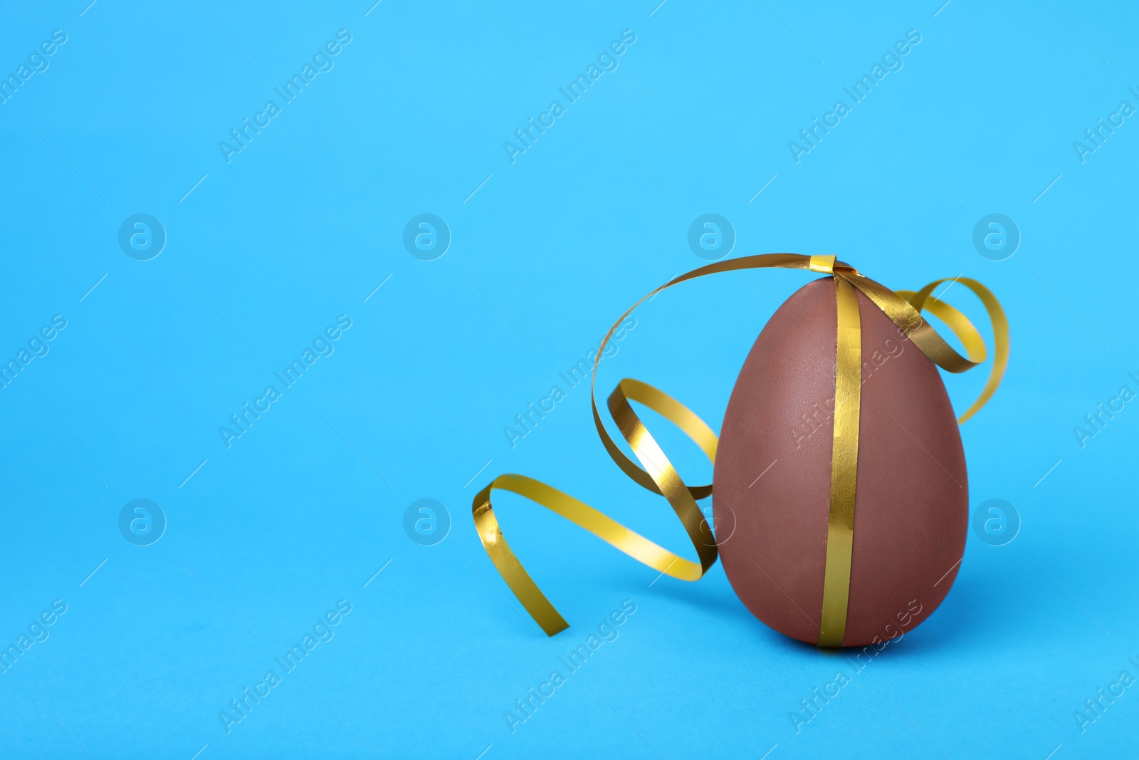 Photo of Delicious chocolate egg with silver ribbon on light blue background, closeup. Space for text
