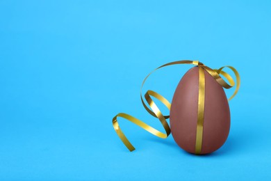 Photo of Delicious chocolate egg with silver ribbon on light blue background, closeup. Space for text