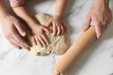 Father and child making dough at white table, top view