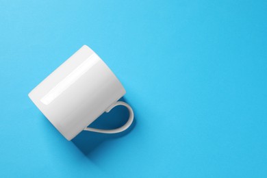 Photo of One white ceramic mug on light blue background, top view. Space for text