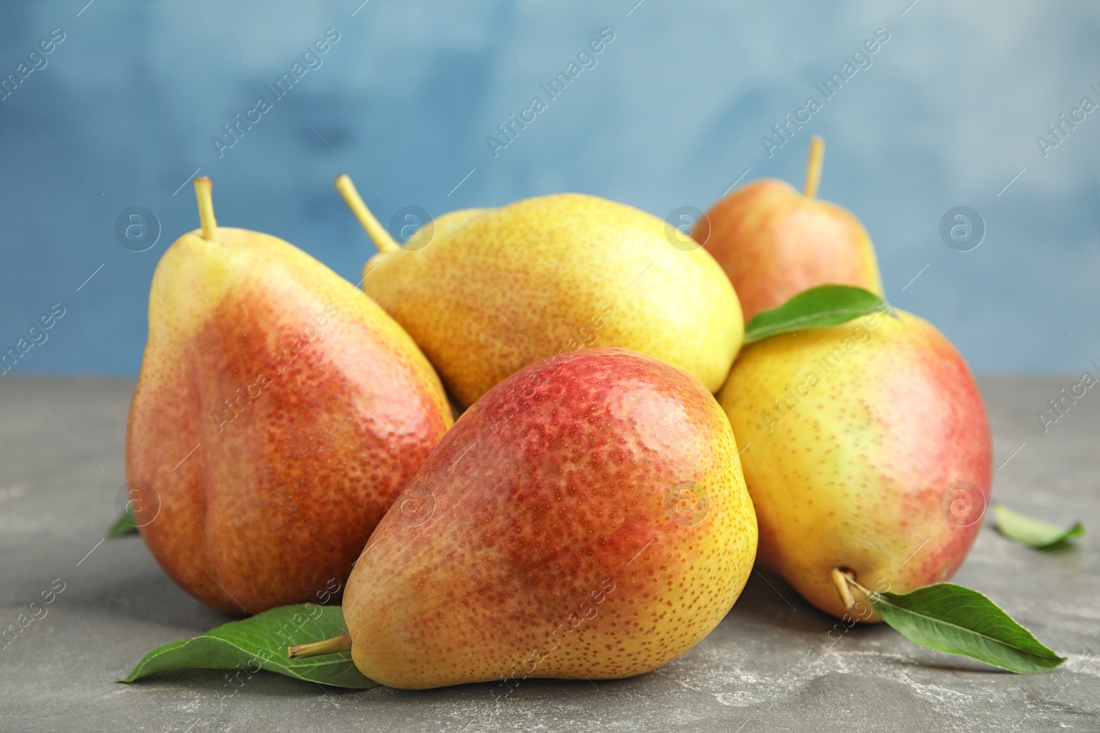 Photo of Heap of ripe juicy pears on grey stone table against blue background