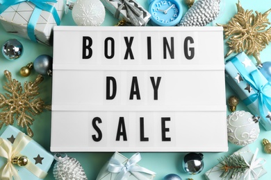 Photo of Lightbox with phrase BOXING DAY SALE and Christmas decorations on light blue background, flat lay
