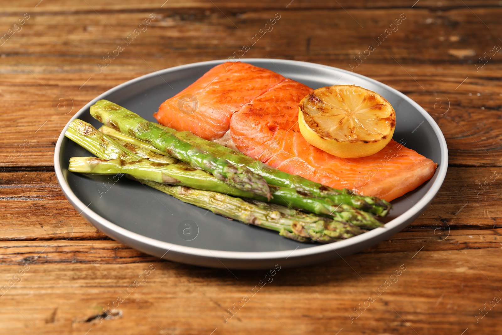 Photo of Tasty grilled salmon with asparagus and lemon on wooden table