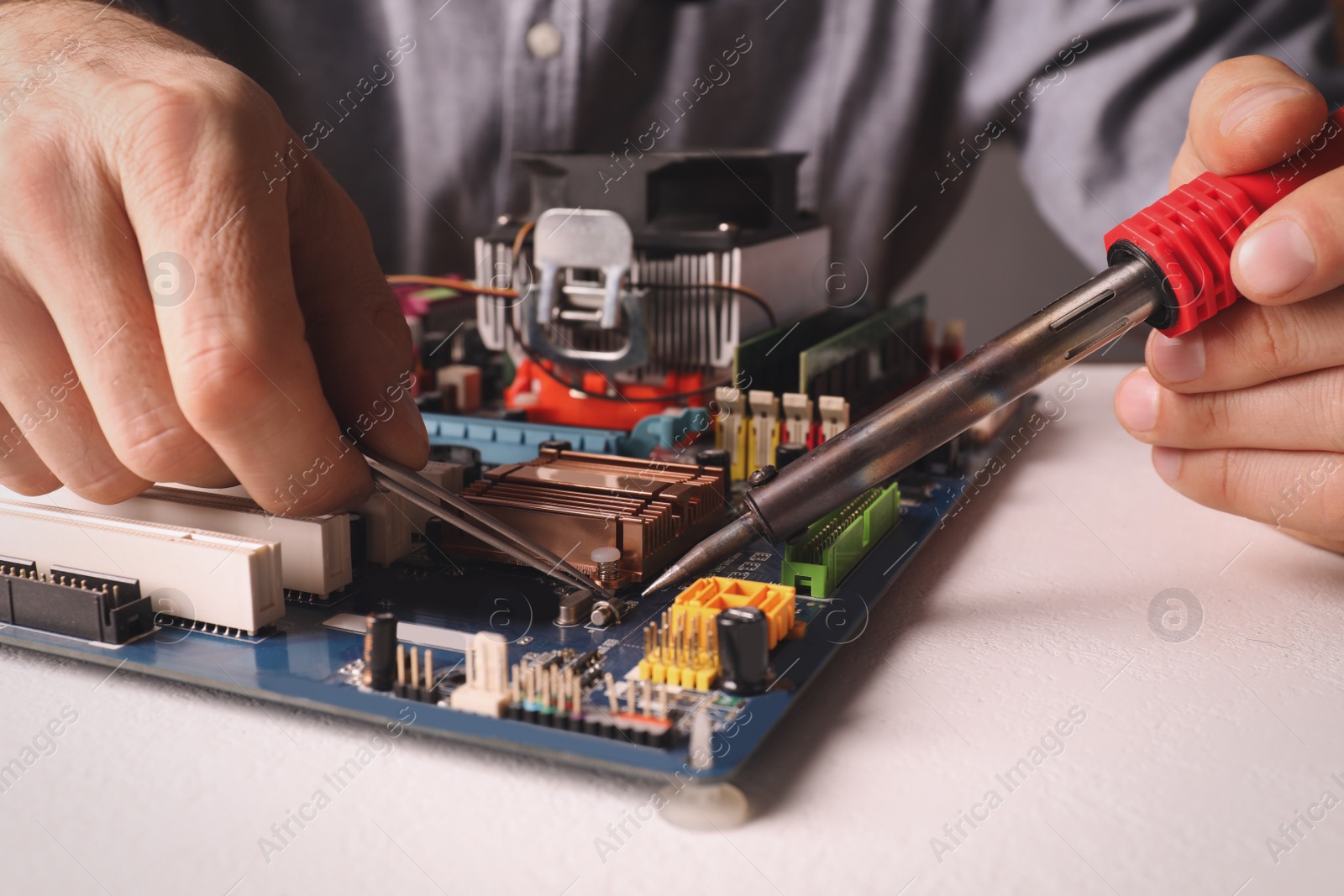 Photo of Technician repairing electronic circuit board with soldering iron at table, closeup