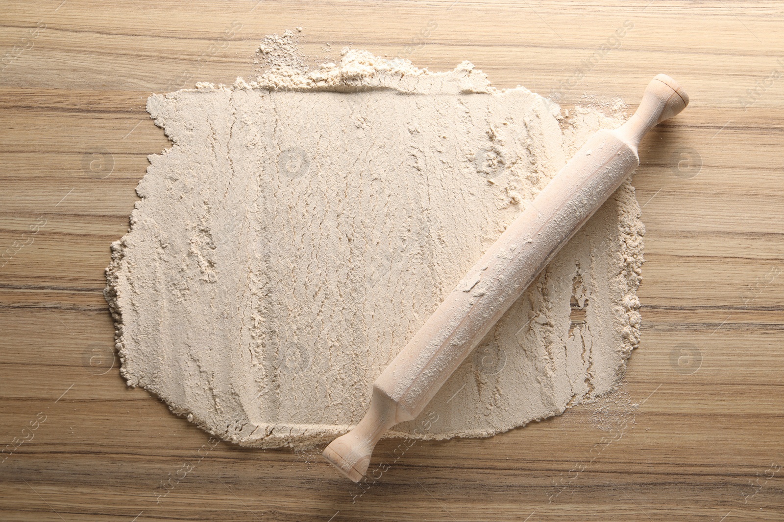 Photo of Flour and rolling pin on wooden table, top view