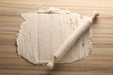 Photo of Flour and rolling pin on wooden table, top view