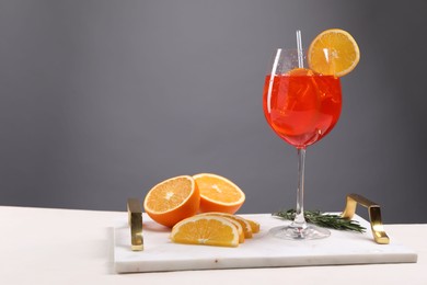 Glass of tasty Aperol spritz cocktail with orange slices and rosemary on white table against gray background, space for text