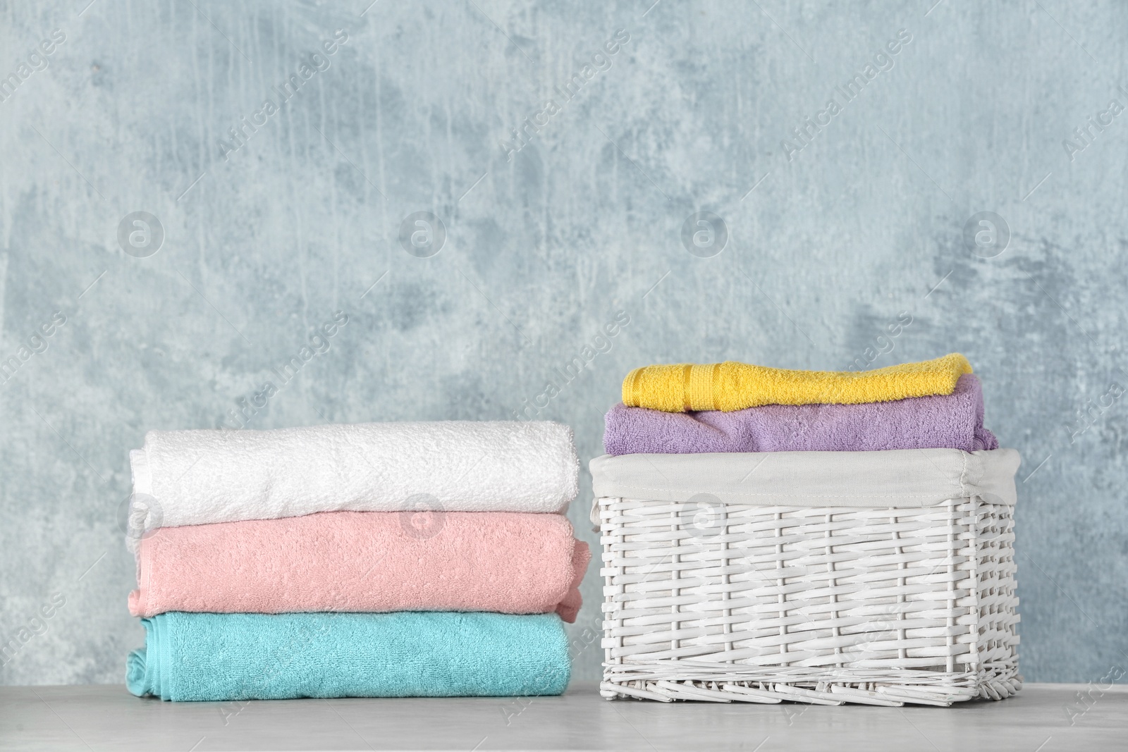 Photo of Basket with clean laundry on table against color background