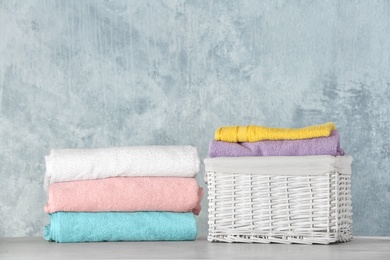 Photo of Basket with clean laundry on table against color background