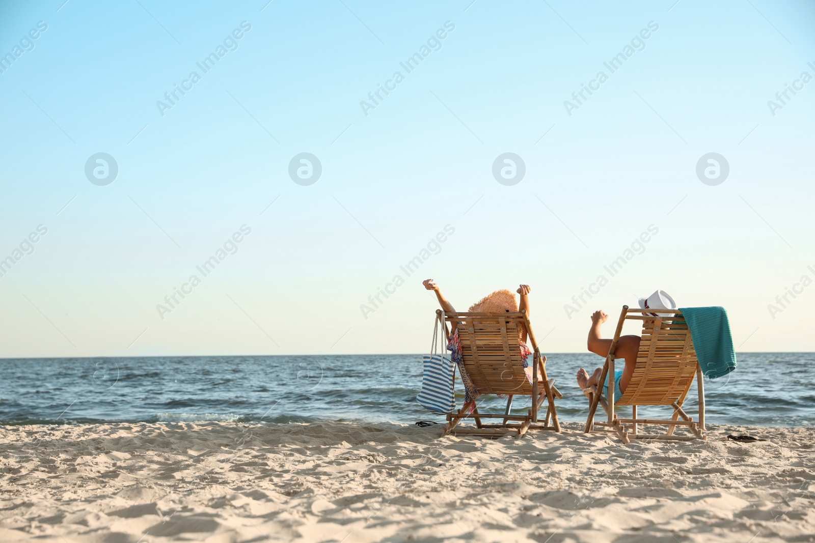 Photo of Young couple relaxing in deck chairs on beach near sea