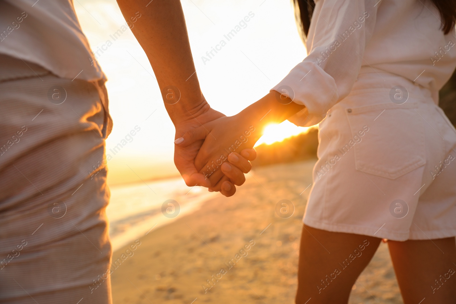 Photo of Lovely couple holding hands on beach at sunset, closeup