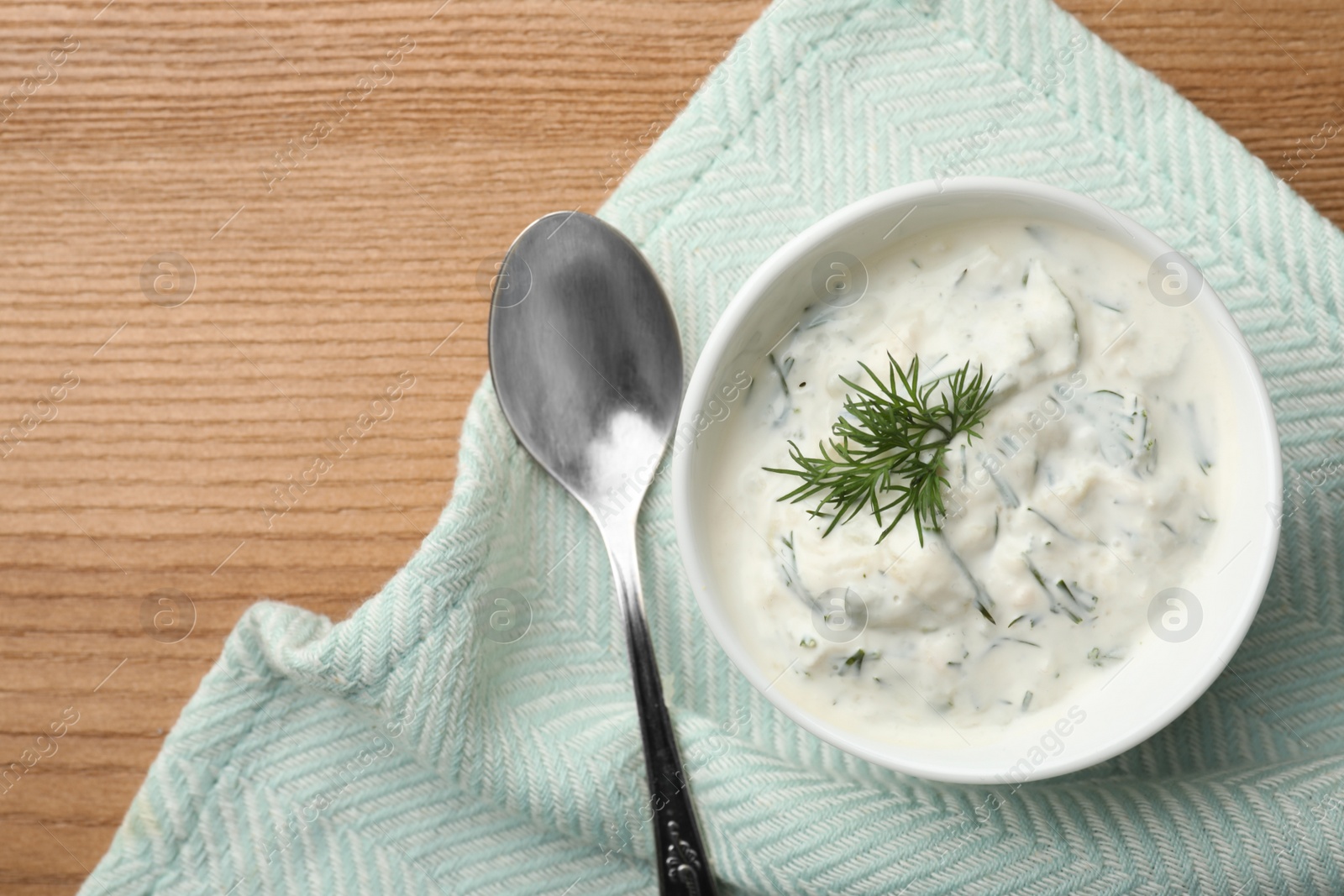 Photo of Cucumber sauce with spoon and space for text on wooden background, flat lay