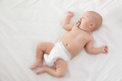 Cute little baby with pacifier sleeping on bed, top view