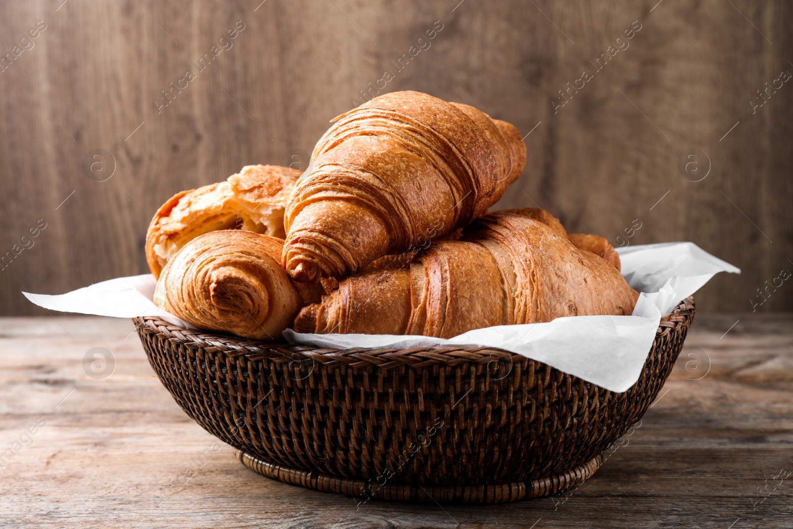 Photo of Tasty fresh croissants in wicker bowl on wooden table