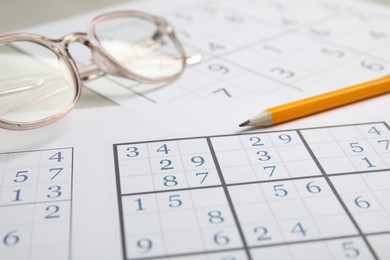 Photo of Sudoku, pencil and eyeglasses on table, closeup view