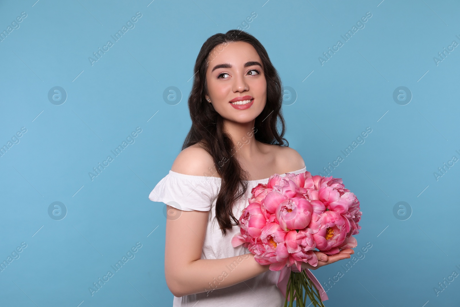 Photo of Beautiful young woman with bouquet of pink peonies on light blue background