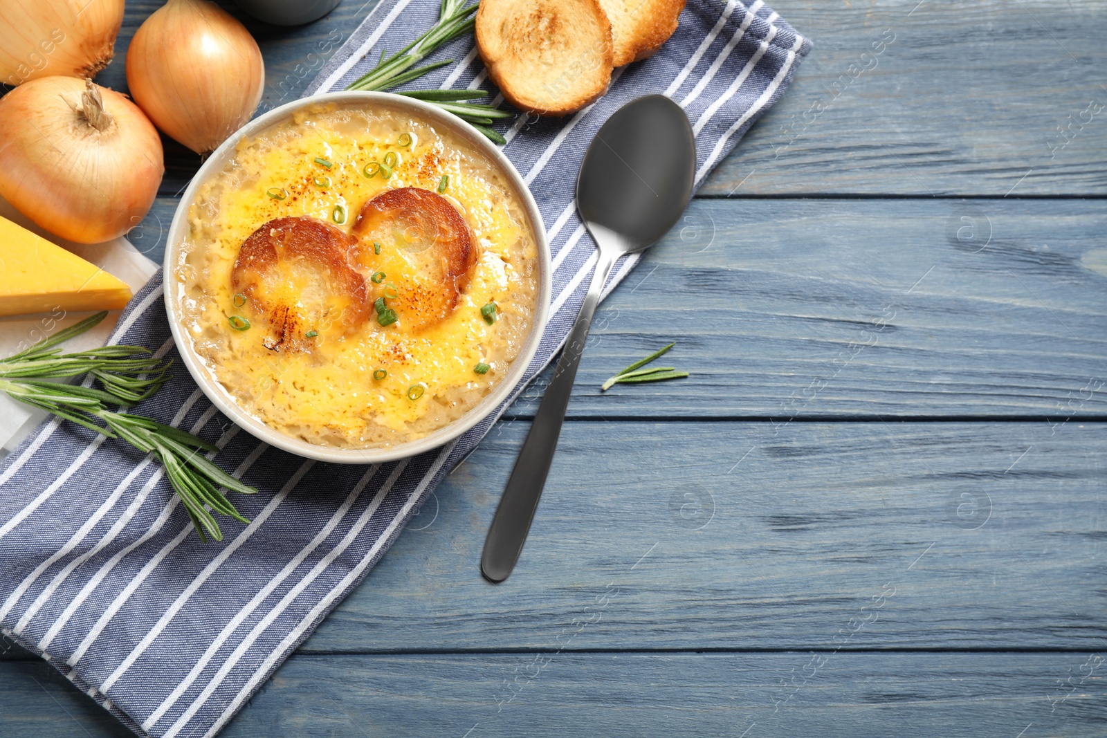 Photo of Tasty homemade french onion soup served on blue wooden table, flat lay. Space for text