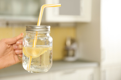 Photo of Young woman with mason jar of lemon water in kitchen, closeup. Space for text