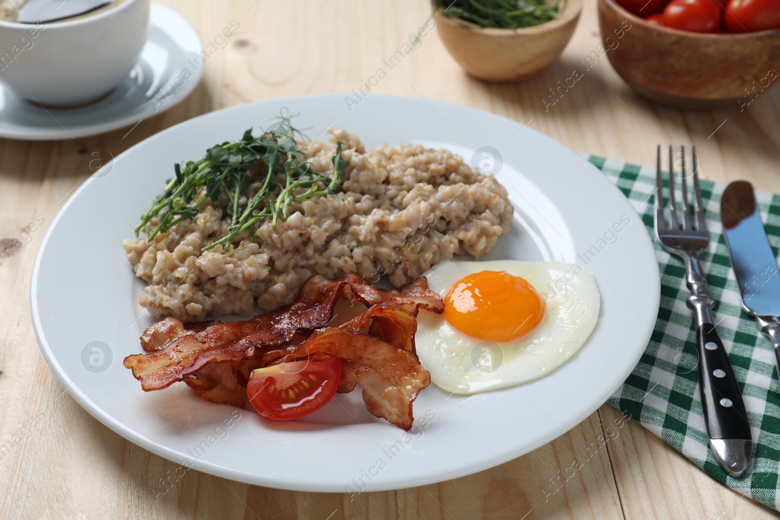 Photo of Delicious boiled oatmeal with fried egg, bacon and tomato served on wooden table, closeup