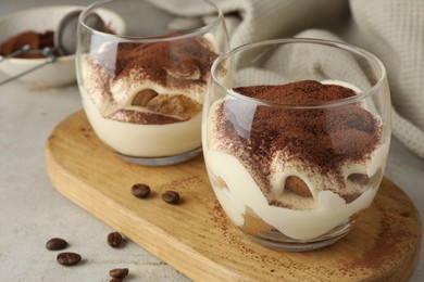 Delicious tiramisu in glasses and scattered coffee beans on light table, closeup