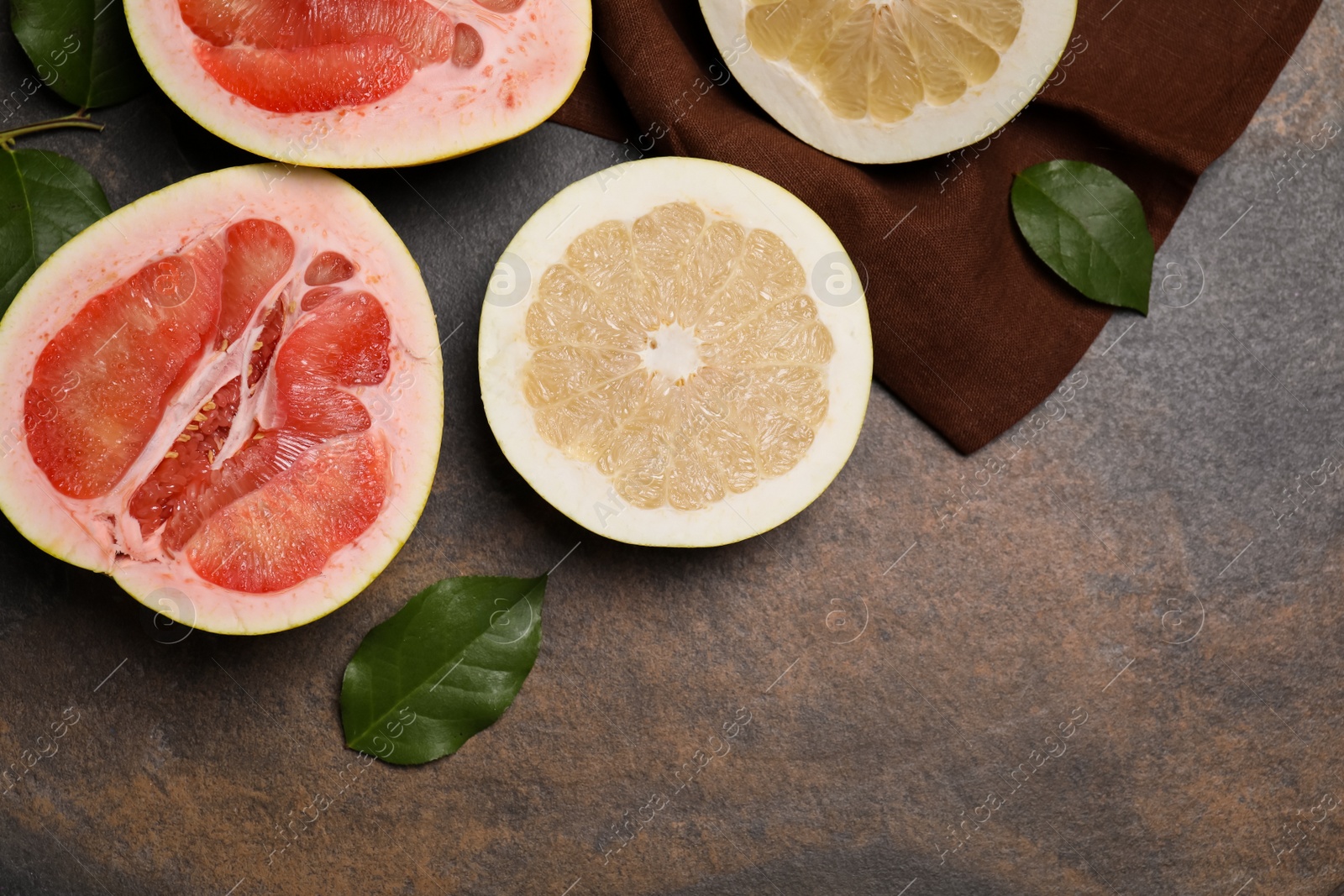 Photo of Fresh cut pomelo fruits with green leaves on dark table, flat lay. Space for text