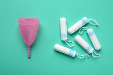 Photo of Menstrual cup and tampons on turquoise background, flat lay