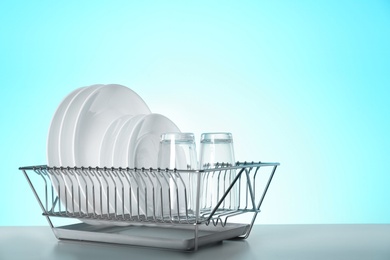 Photo of Drying rack with clean dishes and glasses on table against color background. Space for text