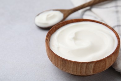 Photo of Delicious natural yogurt in bowl and spoon on light grey table, closeup. Space for text