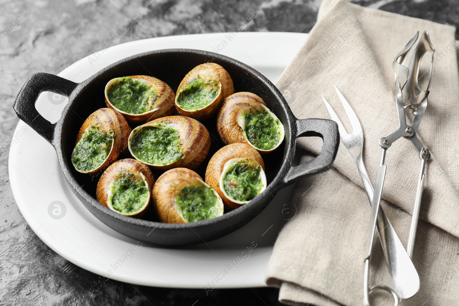 Photo of Delicious cooked snails in baking dish served on grey textured table