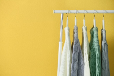 Photo of Collection of warm sweaters hanging on rack near yellow wall, closeup. Space for text
