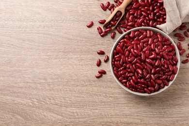 Photo of Raw red kidney beans with bowl, scoop and bag on wooden table, flat lay. Space for text