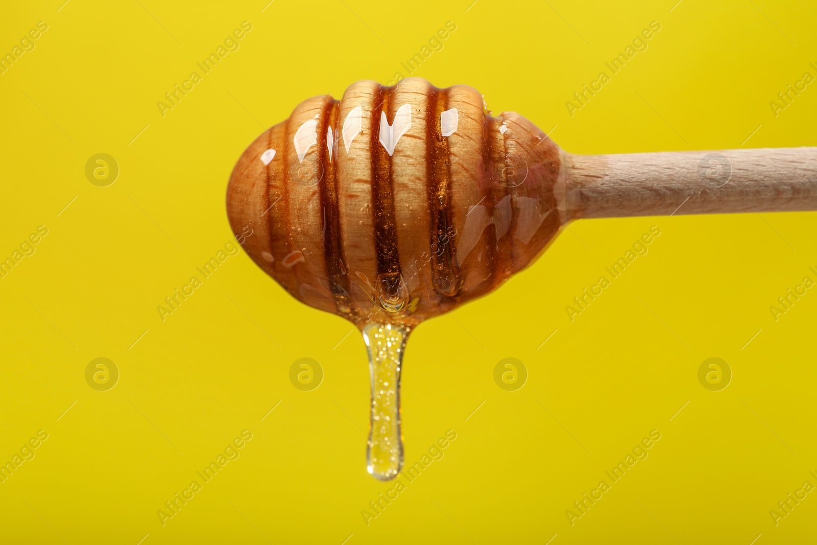 Photo of Delicious honey flowing down from dipper against yellow background, closeup