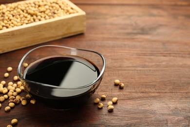Photo of Soy sauce in bowl and soybeans on wooden table. Space for text