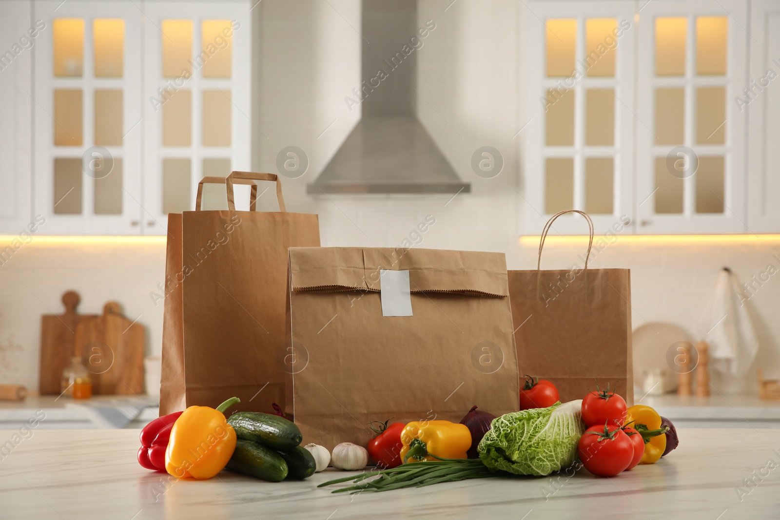 Photo of Paper bags and fresh vegetables on white marble table in kitchen