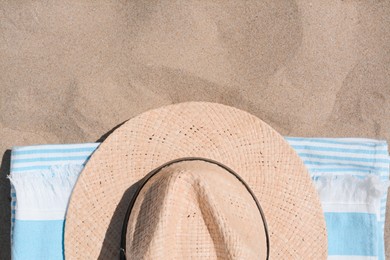 Straw hat and beach towel on sand, top view. Space for text