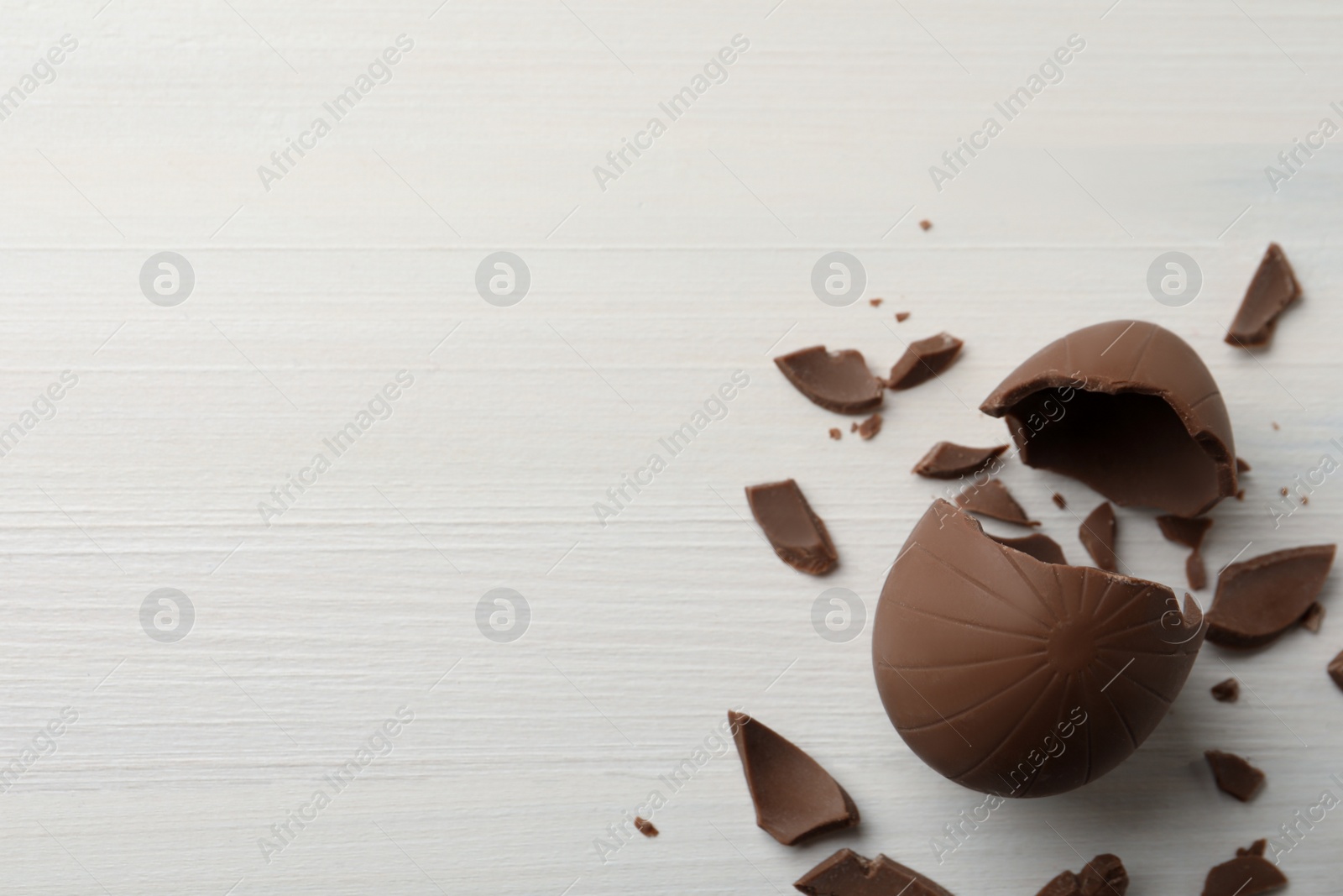 Photo of Broken chocolate egg on white wooden table, flat lay. Space for text