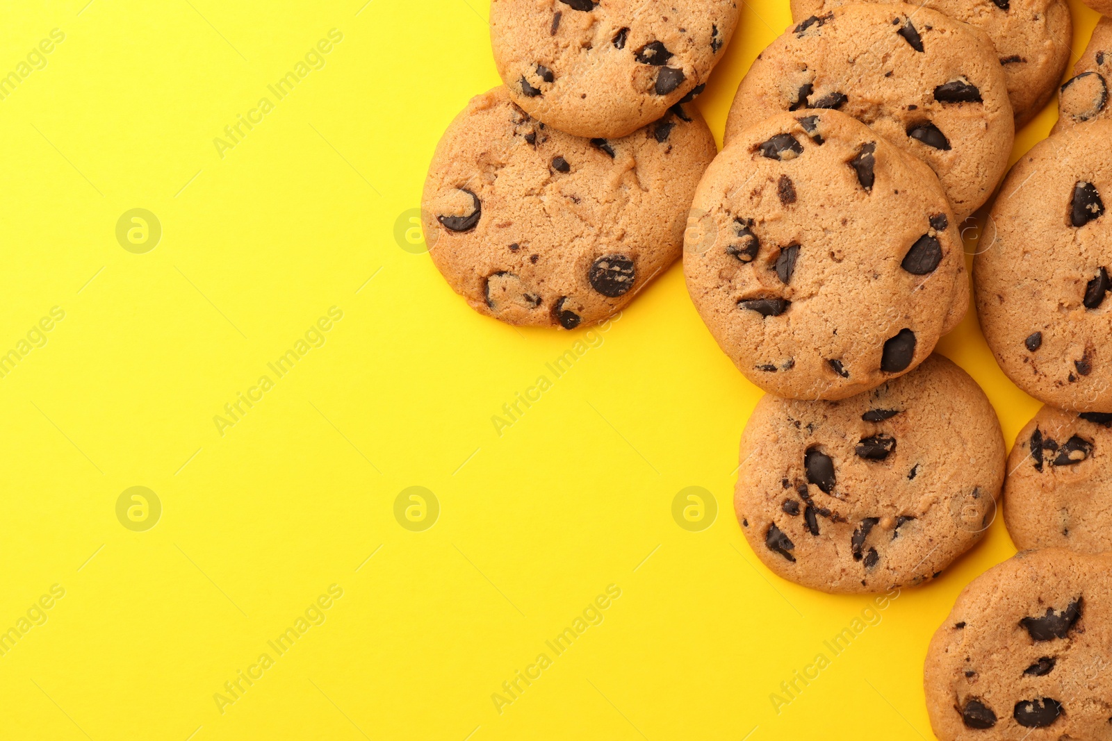 Photo of Many delicious chocolate chip cookies on yellow background, flat lay. Space for text